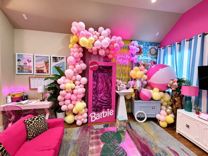 Pink Barbie-themed room with a life-size Barbie box, a balloon garland and neon signs